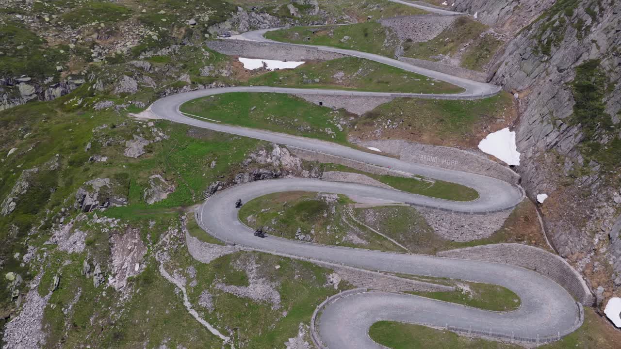 Winding alpine road cutting through rocky terrain with remnants of snow along edges