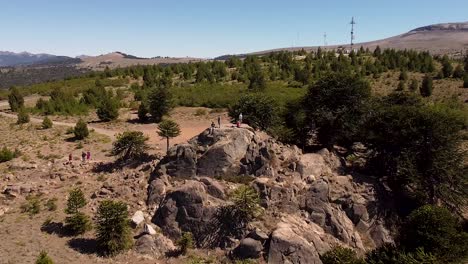 People-are-standing-on-a-rock-cliff,-surrounded-by-untouched-natural-landscape-during-sunshine-day,-distancing-aerial-view,-captured-at-Patagonia,-Argentina,-South-America