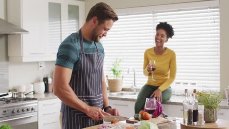 video de una feliz pareja diversa preparando comida, bebiendo vino y divirtiéndose en la cocina