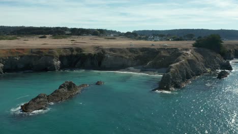 Flying-over-aqua-colored-ocean-water-towards-the-coastline