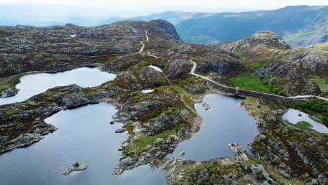 Panoramic-aerial-overview-above-presa-los-garandones-winding-road-and-calm-alpine-lakes