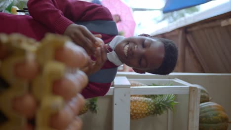 vertical view of vendor giving an organic egg to a boy wearing uniform in market stalls