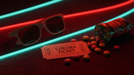 a close-up view of a cinema ticket, colorful candy, and stylish sunglasses beneath neon lights representing the vibe of movie nights and entertainment culture