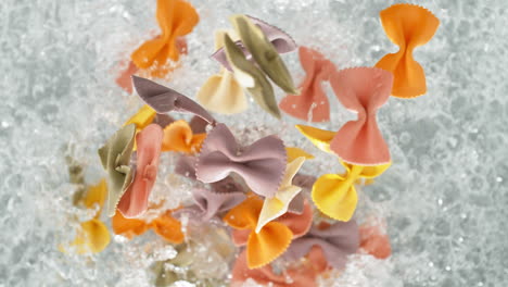 colorful farfalle pasta falling into pot of boiling water making a splash in slow motion, table top view