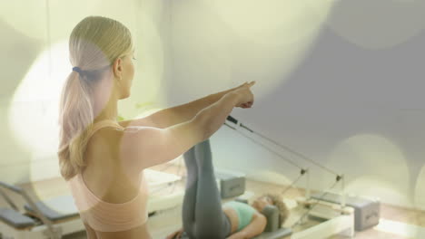 woman pointing while another exercises on reformer machine, fitness animation over