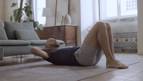 focused caucasian man exercising abs on floor at home