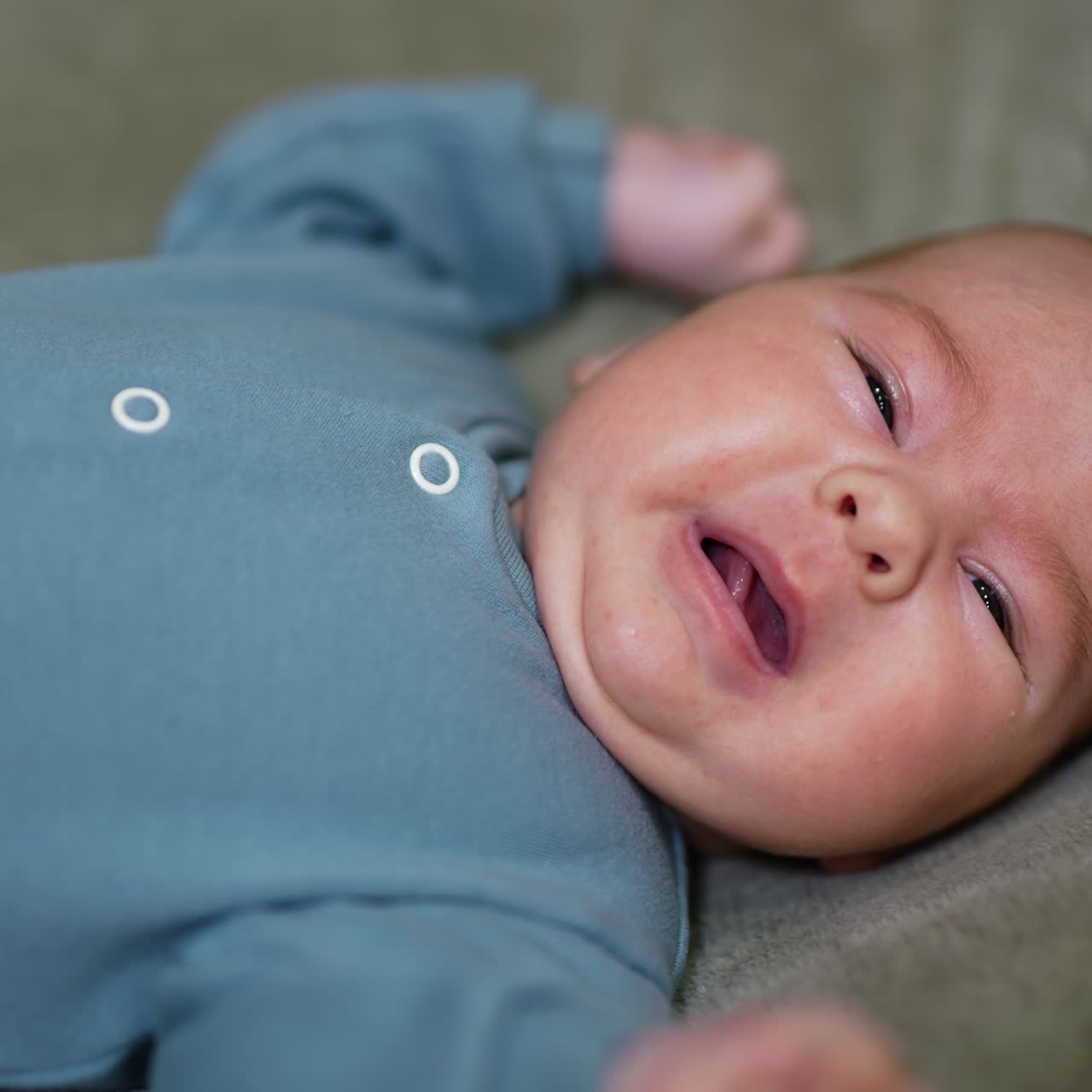 Beautiful infant boy with plump cheeks lies on his back. Little baby wants to start crying but stops suddenly. Close up
