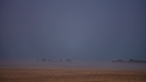 Una-Niebla-Brumosa-Se-Arrastra-Sobre-Las-Tierras-De-Cultivo-Y-Luego-Una-Superluna-Se-Eleva-E-Ilumina-El-Campo---Lapso-De-Tiempo