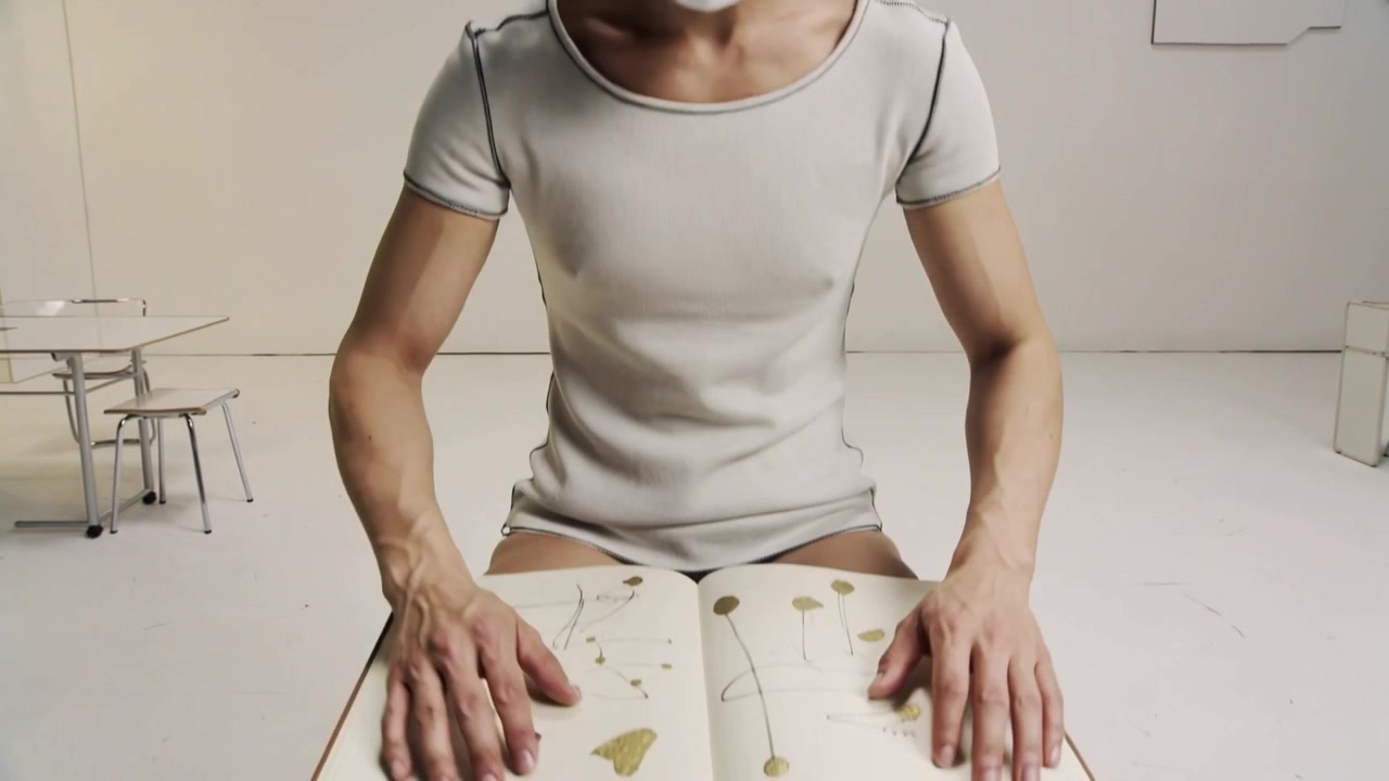 Uomo che si alza con un berretto bianco aderente, posando un libro di botanica sulle ginocchia in uno studio bianco, leggendo.