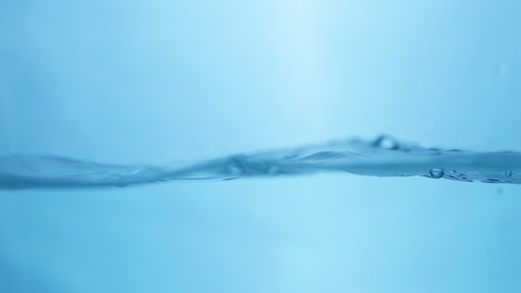 Pouring-into-a-half-filled-container-creating-waves,-ripples-and-droplets-of-water-against-a-blue-background