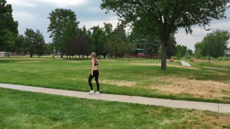 a strong muscular woman walks confidently along a pathway in a park alone. drone 4k