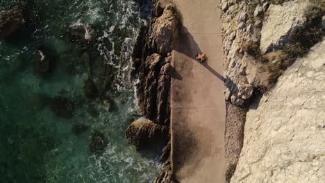 aerial drone eye bird shot of woman walking alone in the coast of baska in croatia in a beautiful sunny day 4k