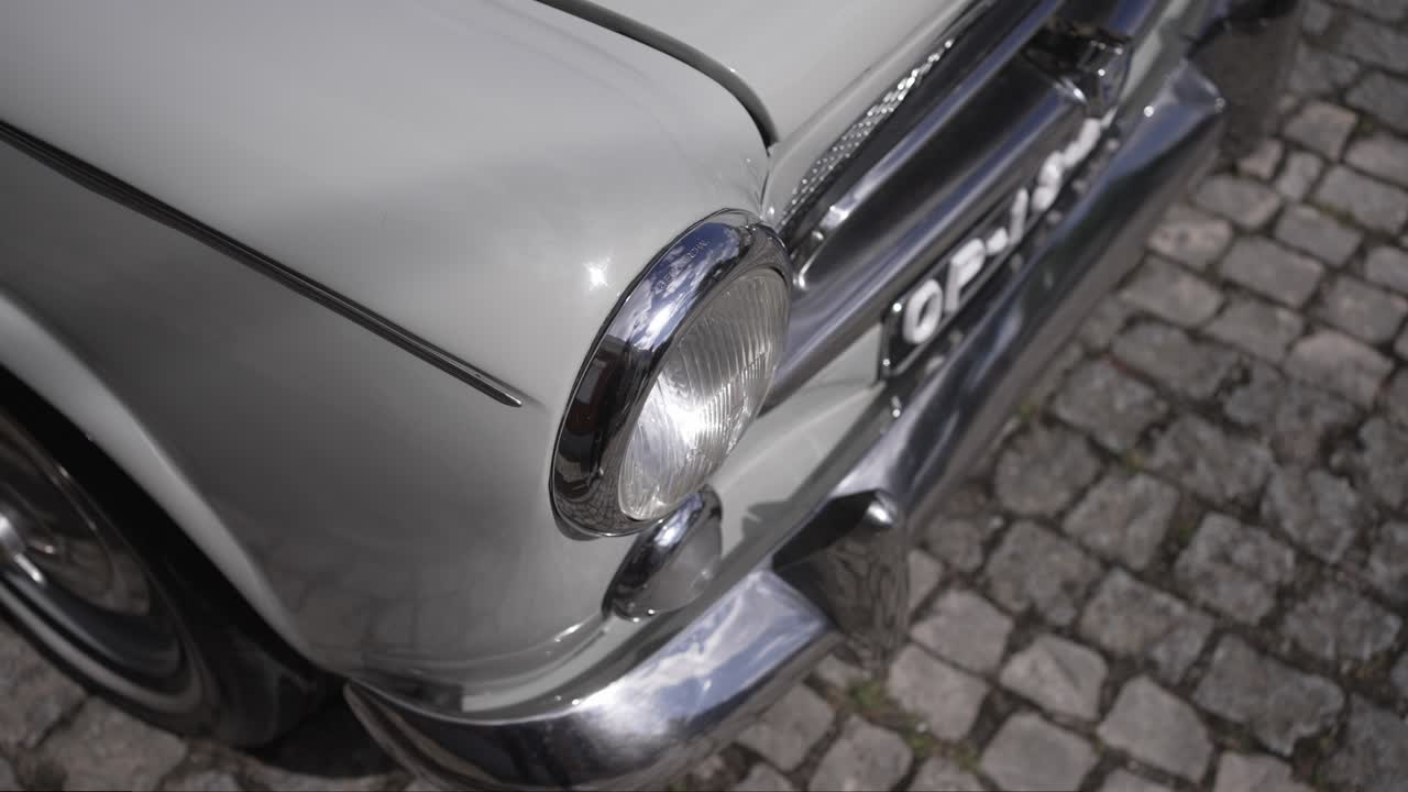 Detail of white vintage car front parked on cobblestone street in daylight