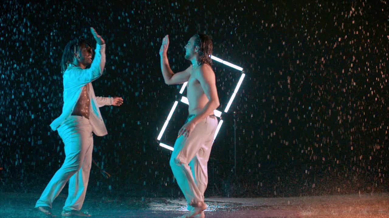 African American and Caucasian Capoeira fighters congratulating and high fiving, indoor rain effect