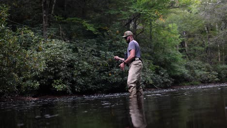 slow motion footage of a fly fisherman casting his line and lure into the stream. the angler is fishing for brook trout or rainbow trout.