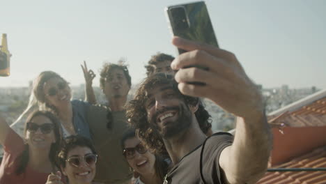 happy bearded man taking a selfie photo with friends during a rooftop party