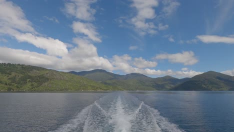 white-water from boat contrasts with lush-green landscape and clouds in summertime - endeavour inlet, marlborough sounds