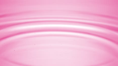 water drop falls down on pink fluid surface creating water rings