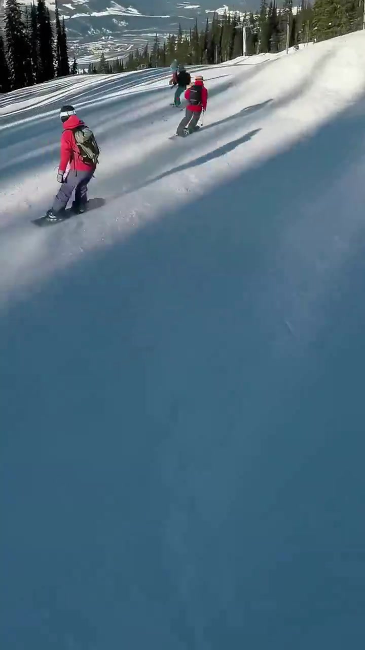 Video verticale: La troupe avvista sciatori e filma uno snowboarder con giacca rossa che intaglia una pista battuta con la tavola.