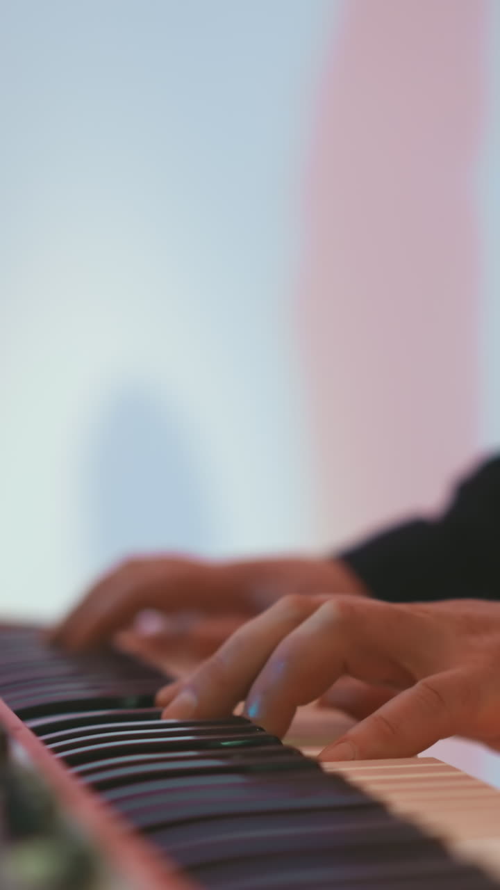 primer plano de las manos de un tecladista tocando un piano de muestreo rojo contra un fondo rosa y azul suave