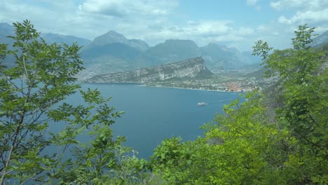 a boat glides across lake garda amidst bushes, under a blue sky, with lush greenery, italy
