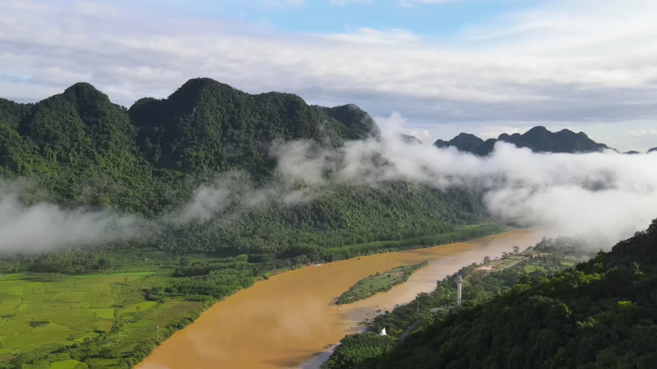 Drone shot revealing beautiful flooded brown river with cloud lingering above and green limestone mountain range at the background in Phong Nha Viet Nam