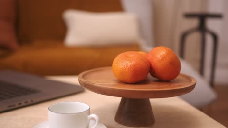 two oranges on wooden cake stand beside white mug and laptop