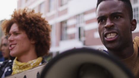 hombre afroamericano gritando usando megáfono con otras personas levantando los puños durante la protesta