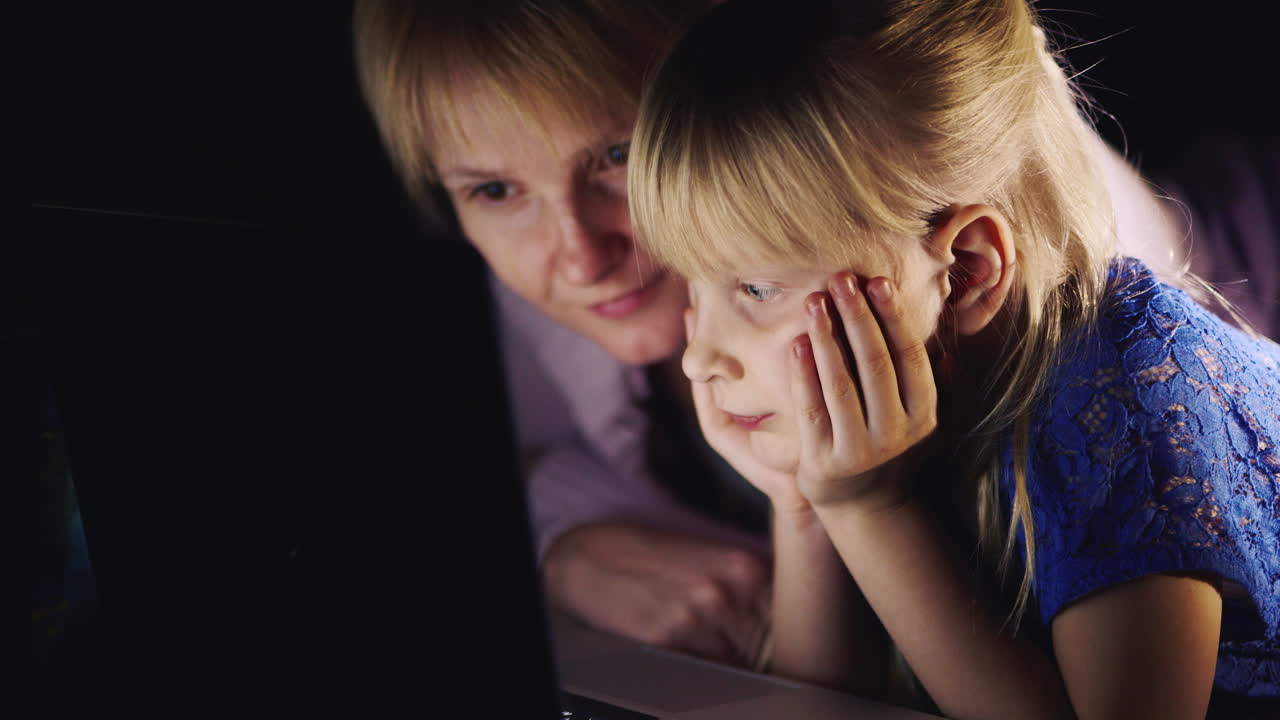 Mother And Daughter Lying On The Bed Use A Laptop