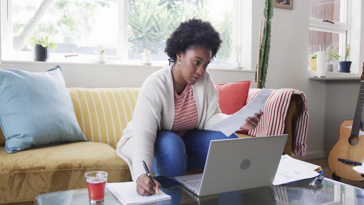 Donna afroamericana concentrata che lavora da casa, sbrigando pratiche amministrative e usando il laptop, al rallentatore