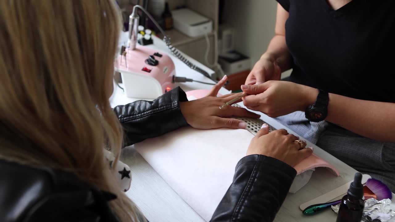 Master polishing nails of female customer with electric file