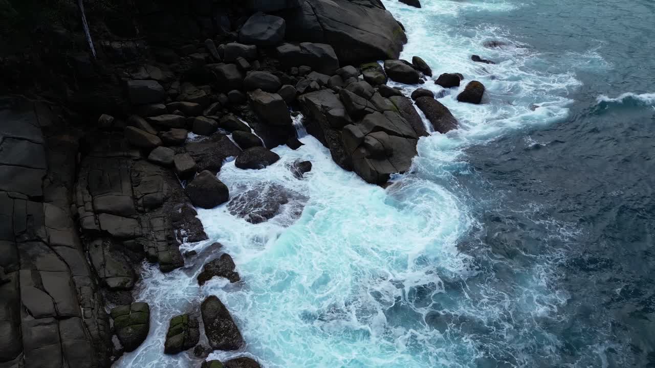 Aerial shot capturing powerful waves crashing onto the rugged rocks along the coastline in Mahe, Seychelles. dolly shot