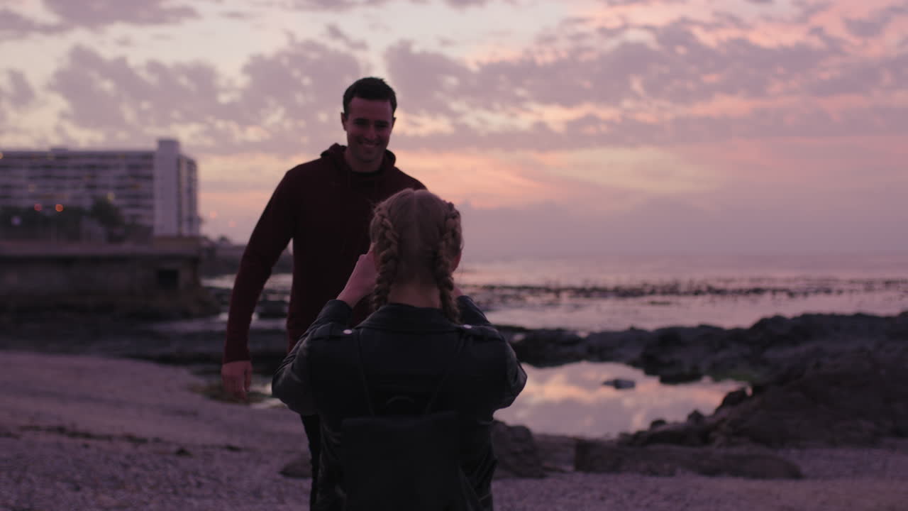 joven pareja divirtiéndose tomando fotos en la playa hombre posando brazos levantados feliz alegre