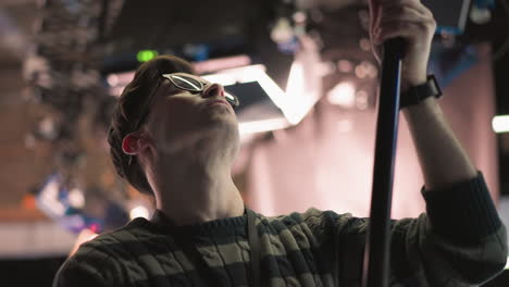 close-up of man adjusting boom microphone in professional studio, focusing on equipment, sound recording process in action, preparing for video production with lighting and crew visible