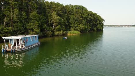 person canoeing to a house boat on a green natural lake next to a forest in brandenburg, germany