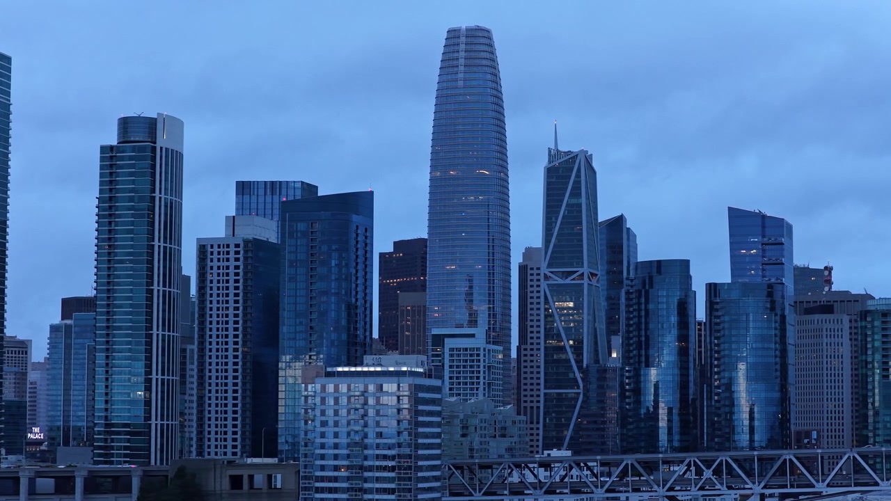 Skyline di San Francisco al tramonto con l'iconica Salesforce Tower e imponenti grattacieli di vetro. L'illuminazione dell'ora blu evidenzia l'architettura moderna in una ripresa cinematografica grandangolare del paesaggio urbano.