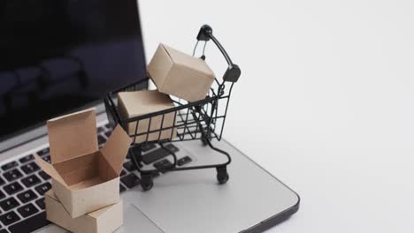 Video-of-laptop-with-blank-screen,-shopping-trolley-and-boxes-with-copy-space-on-white-background