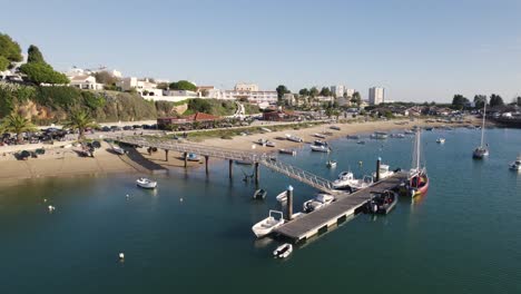 Barcos-De-Pesca-En-El-Muelle-De-Madera-A-Lo-Largo-De-La-Orilla-Del-Río-En-Alvor,-Portugal,-En-órbita-Aérea