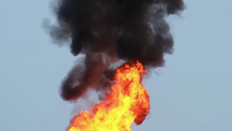 Close-up,-Hot-Flames-with-black-billowy-smoke-against-blue-sky