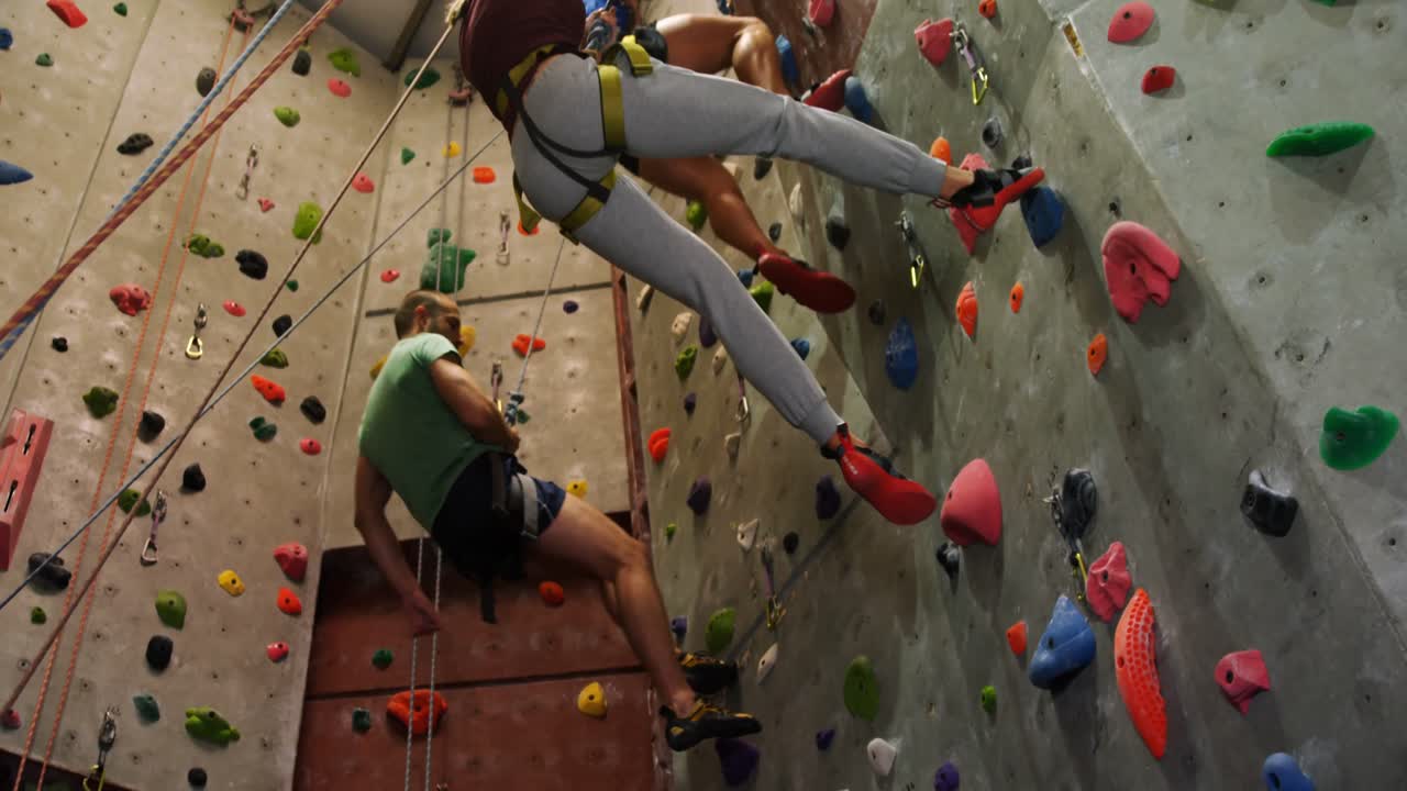 hombres y mujeres escalando una pared artificial en el gimnasio de bouldering 4k