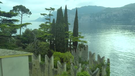 experience lush vegetation and majestic cypress trees framing lake garda against the backdrop of italy's veneto and lombardy regions