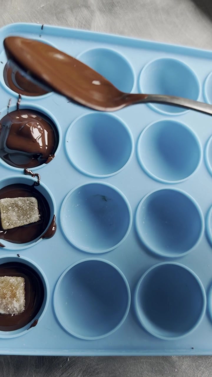 Primo piano di pezzi di zenzero fatti in casa ricoperti di cioccolato fuso in uno stampo di silicone, che mostra un semplice dolcetto e la preparazione di cibo casalingo.