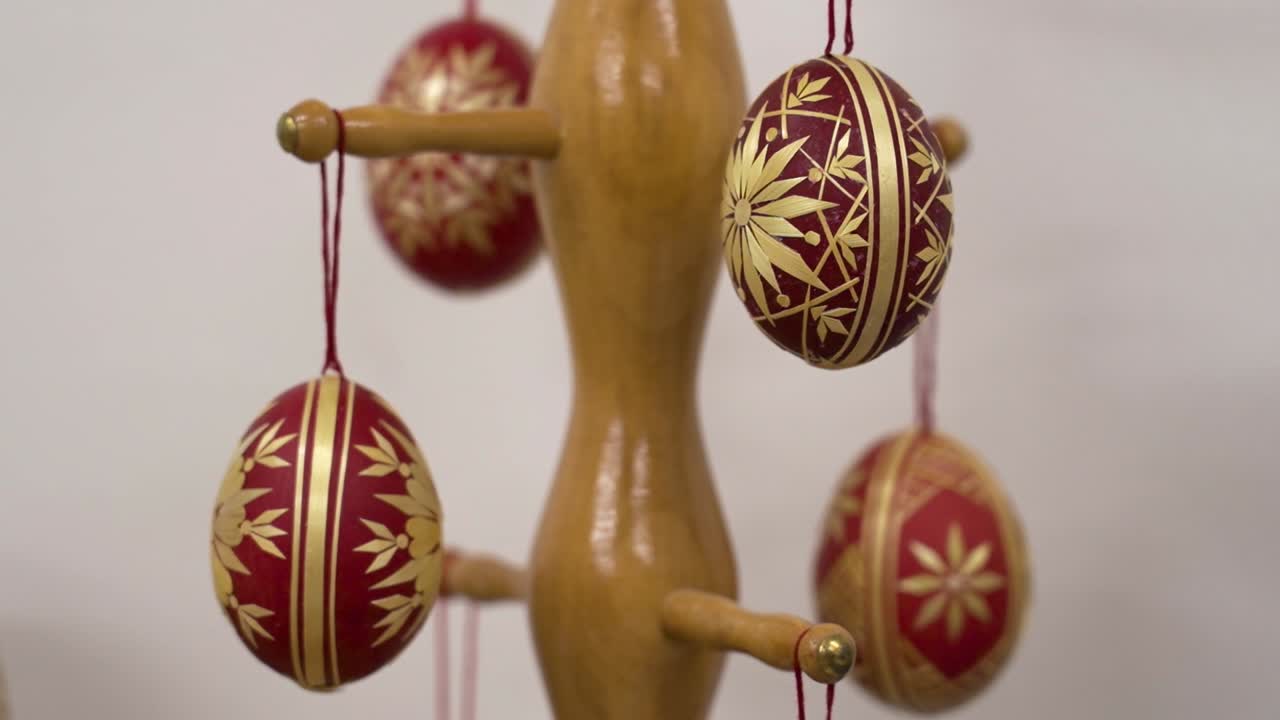 Red and gold traditional Easter eggs hanging from a wooden display stand