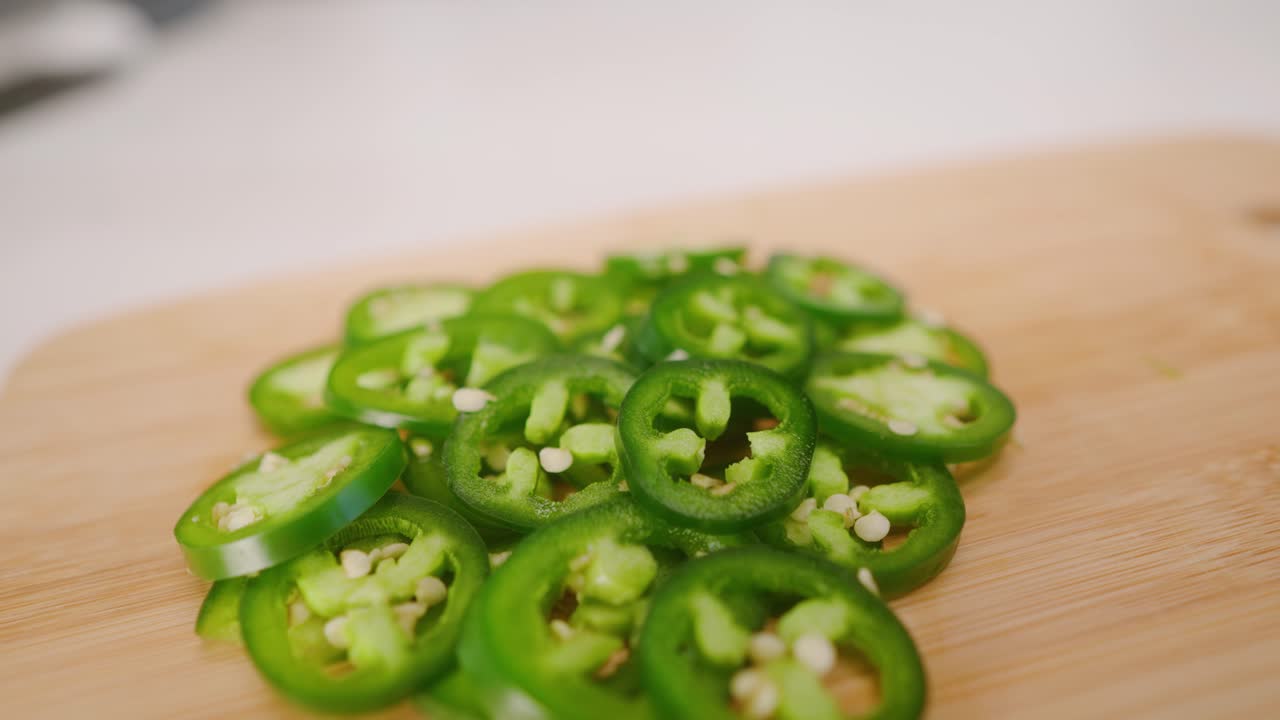 부엌에 있는 커팅 보드에 있는 갓 자른 jalapeños의 밝은 녹색 더미를 가로지르는 슬로우 모션 드리프트