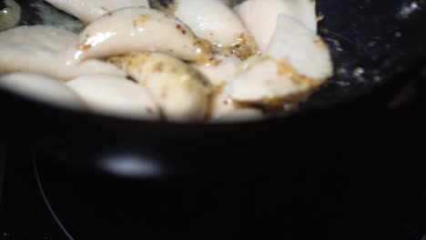 slow motion large dumplings flipped in hot pan being coated with herbs and oils