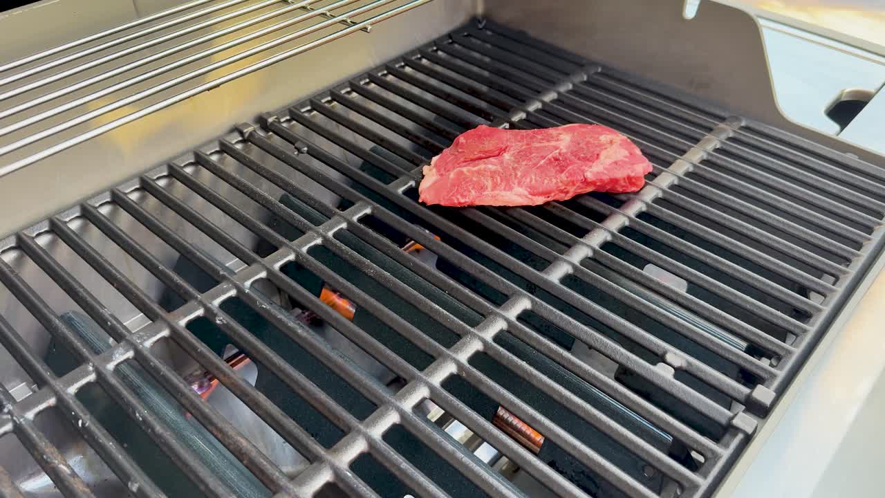 A person uses tongs to place raw wagyu beef steaks onto a clean outdoor gas barbecue grill in bright natural daylight, focusing on preparation