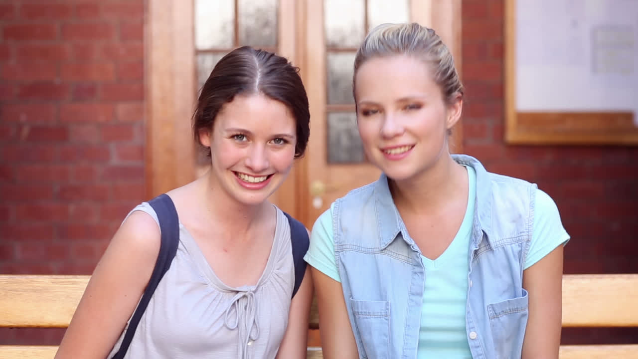 compañeros de clase sentados en un banco usando una computadora portátil juntos