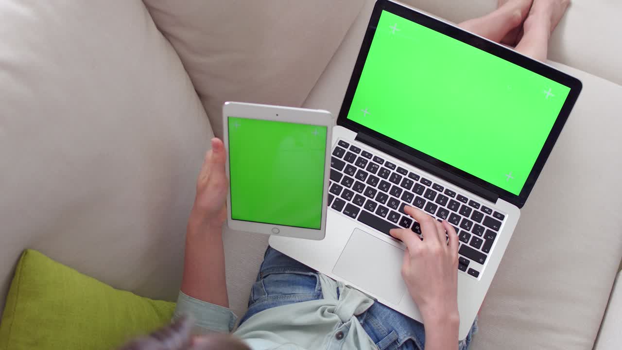 hermosa chica usando una tableta pc y una computadora portátil con pantalla verde pre-enclavada sentada en el sofá en casa.