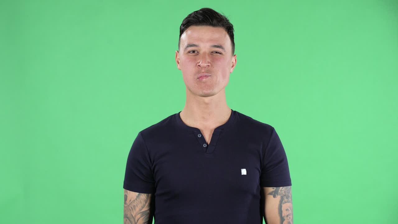 Portrait of a handsome young guy looking straight smiling and showing a heart gesture and air kissing. Green screen