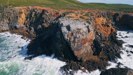 rugged coastal cliff washing by stormy foamy ocean sunny day. drone rough sea